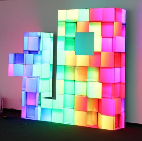 Vivid LEDCON SL-3.75SI Rent LED Wall Module 3.75mm Ecke 90° panels create a bright, geometric Tetris-style wall display, with modular sections glowing in pink, blue, green, and yellow against a plain background—ideal for eye-catching digital signage and event backdrops.