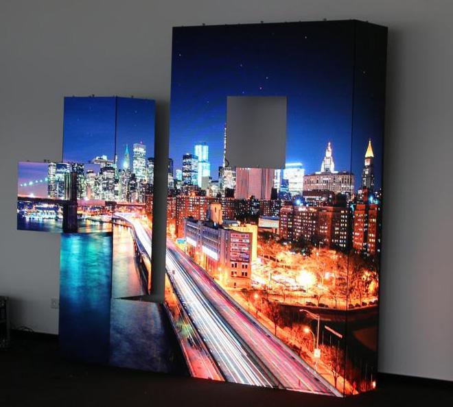Large LEDCON SL-3.75SI 3.75mm Ecke 90° LED wall modules display a vibrant night cityscape with colorful traffic light trails against a plain wall; two rental LED panels feature square cutouts, creating visible gaps in the seamless city image.