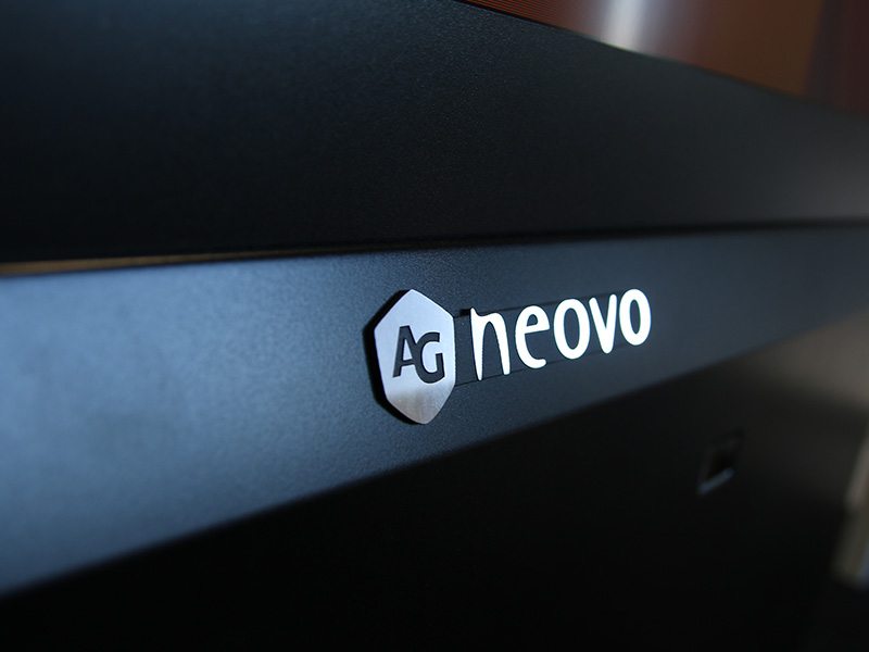 Close-up of an AG Neovo black monitor, featuring the brand name AG neovo in silver letters on the matte surface. The image highlights the sleek design and modern finish of the electronic display device.