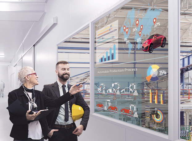 Two business professionals stand in front of a glass wall displaying virtual charts, graphs of automobile production, exports, and a world map with statistics, inside a modern factory. The image highlights advanced automotive manufacturing analytics and global industry data in an innovative workspace.