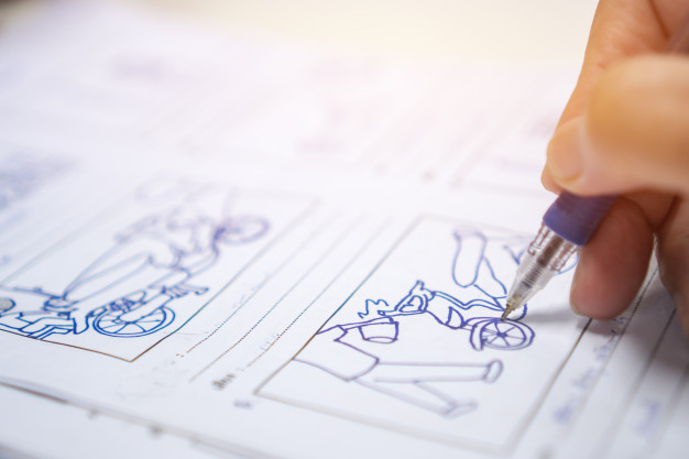 Close-up of a hand holding a pen and drawing a blue outline of a bicycle and rider on a worksheet with multiple cartoon illustrations. Ideal for educational activity books or creative drawing worksheets for kids.