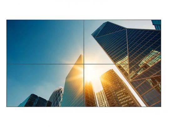 Tall modern skyscrapers with glass facades, such as office buildings or high-rise apartments, reflect sunlight against a clear blue sky. The photo is taken from below, looking up at the towers with the sun shining brightly between them.