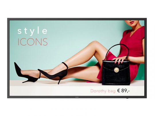 Woman in red dress with black heels holding Dorothy bag – A stylish woman sits with crossed legs, showcasing the black Dorothy handbag (€89) against a light blue and cream background with “style ICONS” text. Fashion product image.