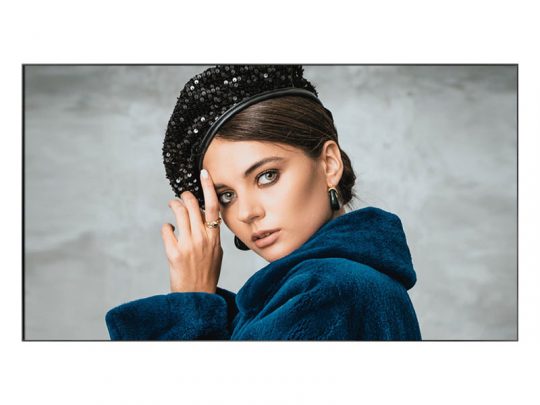 Produktbild einer Frau mit glattem braunen Haar, die einen blauen Kunstpelzmantel und ein schwarzes, paillettenbesetztes Barett trägt. Sie blickt direkt in die Kamera und berührt mit einer Hand ihren Kopf. Große Creolen-Ohrringe runden das trendige Outfit ab. Dieser modische Look-blauer Faux Fur Mantel und schwarze Glitzer-Mütze-ist jetzt zum Kaufen oder Mieten erhältlich, ideal für besondere Anlässe.