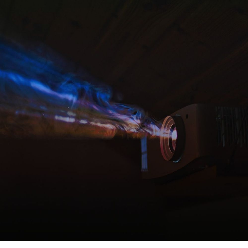 Beamer mieten in Nahaufnahme im dunklen Raum: Der Projektor strahlt leuchtende blaue und violette Lichtstrahlen aus.